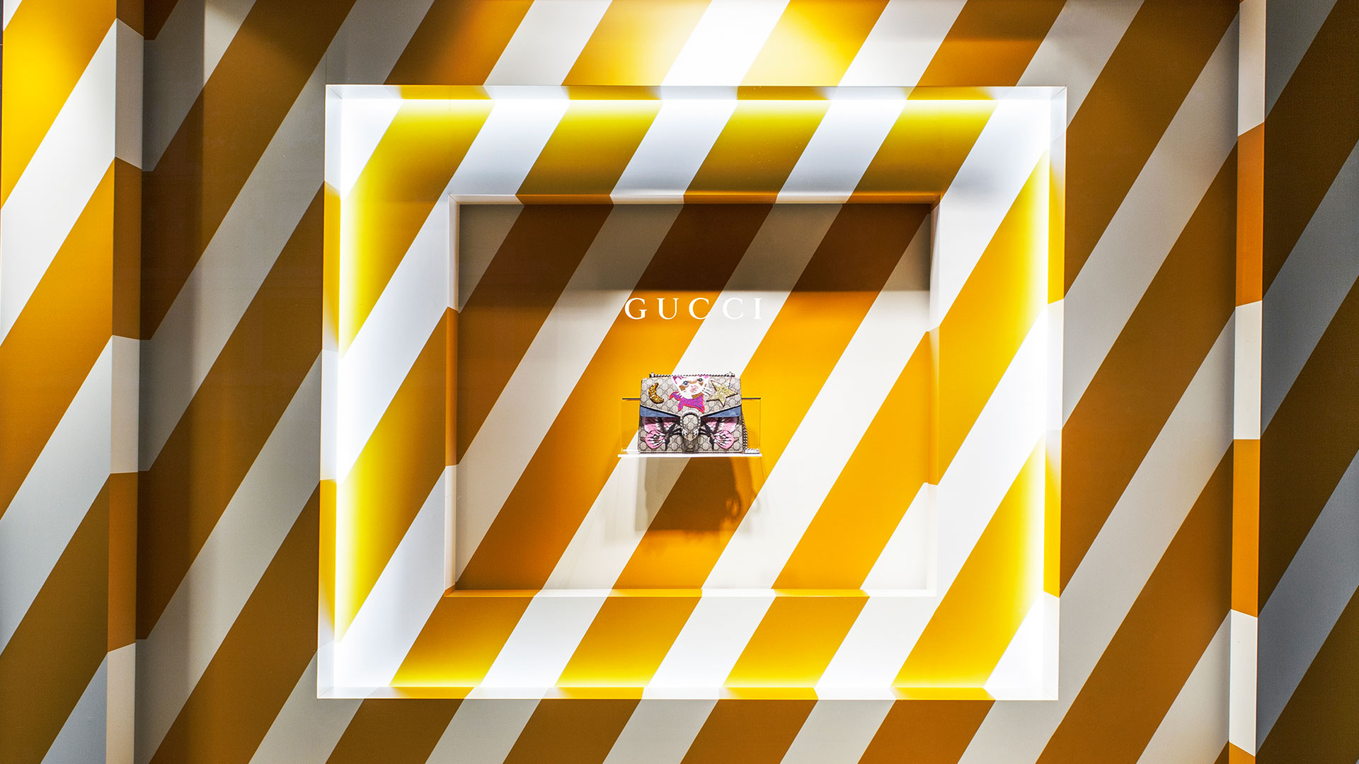 Breuninger Schaufenster mit Gucci-Display in gelb-weißem gestreiften Rahmen, kreiert von MORE PIOUS STUDIOS für POS & Window Campaign.