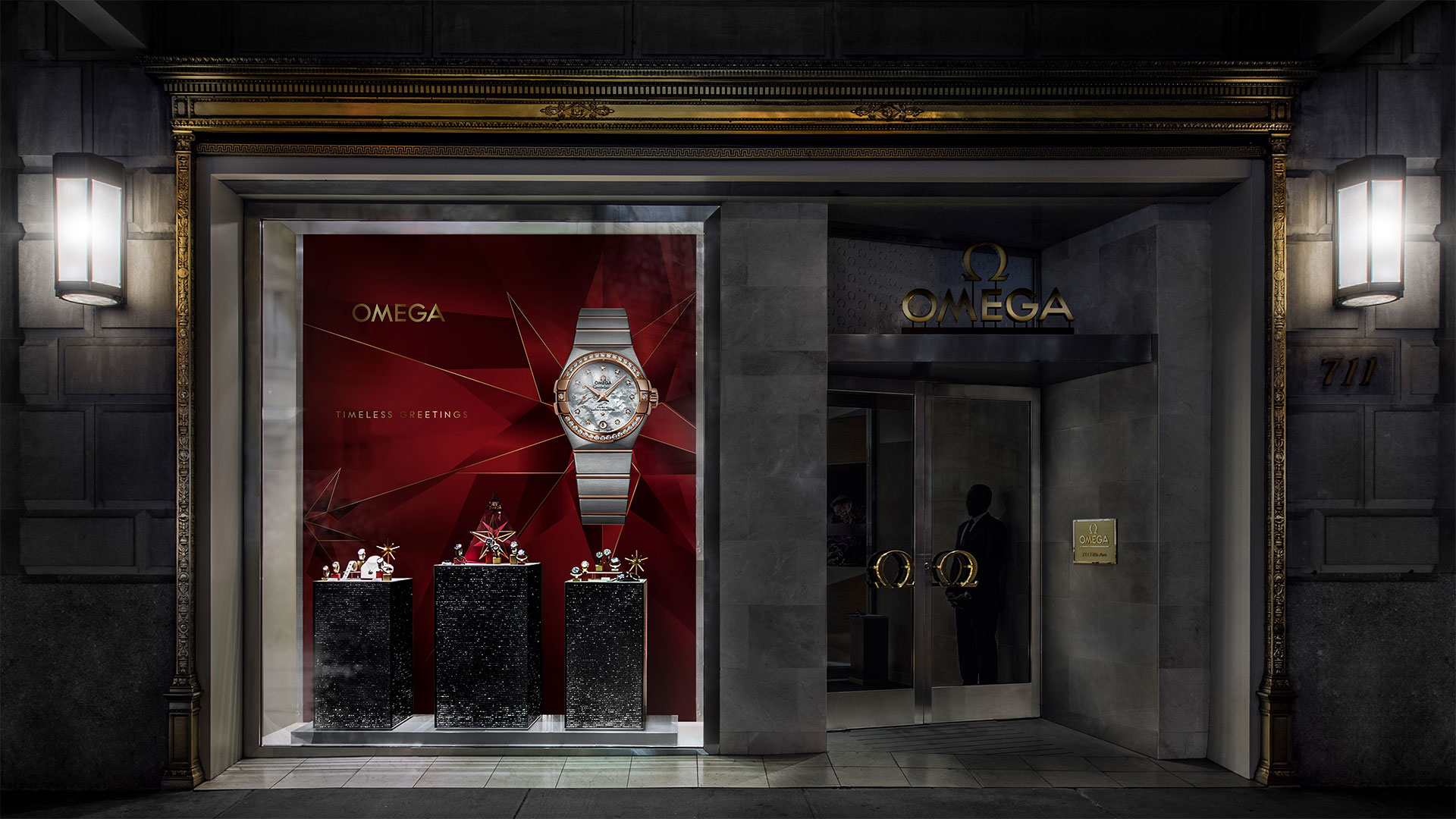 Nachtsicht eines Omega-Schaufensters mit beleuchtetem Display, das eine festlich dekorierte Uhr und rote Sternmotive zeigt.